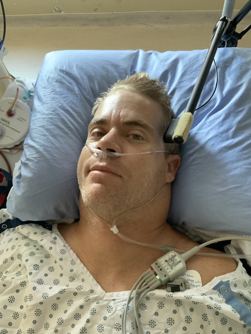 Jason Moore in a hospital bed with a nasal cannula and monitor leads, days after spinal surgery in 2022